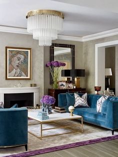 a living room filled with blue couches and chairs next to a fire place under a chandelier