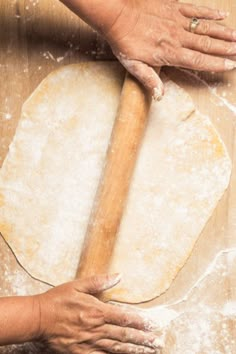 two hands rolling out dough on top of a wooden table next to a rolling pin