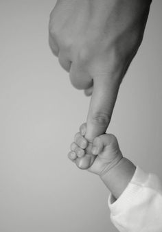 a black and white photo of a person holding a baby's hand