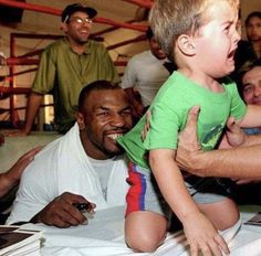 a man holding a small child in front of him while others look at him and smile