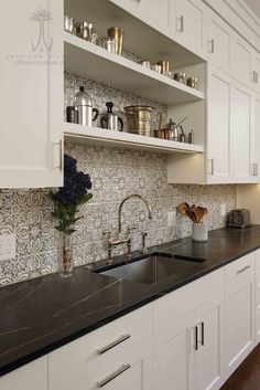 a kitchen with white cabinets and black counter tops is pictured in this image, there are many pots on the shelves above the sink