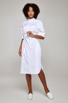 This fashionable  lab coat will make any female doctor or a beautician look stylish and classy when at work.  The elegant uniform dress has a comfortably fitted silhouette of a midi length. It has mockneck and side cuts and fastens with hidden buttons.  The width of the sleeves can be adjusted with the help of buttoned plackets.  The dress is completed with 2 belts that allow changing the dress's look and make the silhouette more elegant and slender.  The fabric is 70% cotton, 30% polyester, mad Nurse Scrub Dress, Beautician Uniform, Lab Coat Fashion, Doctor Clothes, Nurse Style, Medical Scrubs Fashion, Scrub Uniform, Nurse Dress Uniform, Doctor Coat