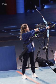 a woman is shooting an arrow with a bow and arrows in her hand while standing on a stage