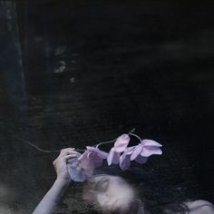 a woman holding flowers in her hands while looking at the ground through a glass window