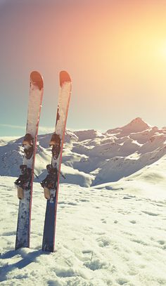 two skis sticking out of the snow in front of a mountain range at sunset