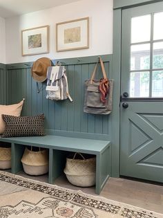 a green bench sitting next to a door with two bags hanging on the wall above it