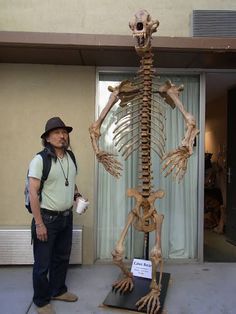 a man standing next to a skeleton in front of a building with a sign on it