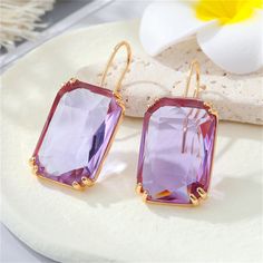 A twinkling pair of drop earrings designed with a radiant-cut crystal in a pastel hue. 0.79" W x 1.57" L 18k gold-plated copper / crystal Lilac Earrings, Cherry Earrings, Beaded Jewels, Gem Earrings, Copper Glass, Purple Rhinestone, Purple Crystal, Colored Gems, Purple Crystals