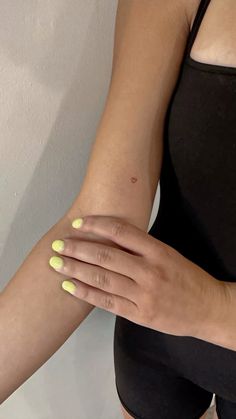 a woman's hand with yellow nail polish holding onto her arm and wearing a black tank top