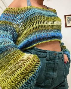 a woman wearing a blue and green crochet sweater with her hands on her hips