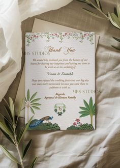 a wedding thank card sitting on top of a bed next to flowers and greenery