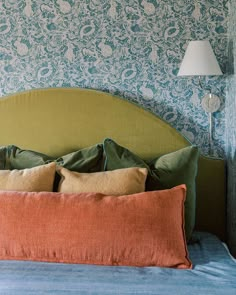 a green headboard with four pillows and a lamp on the nightstand next to it