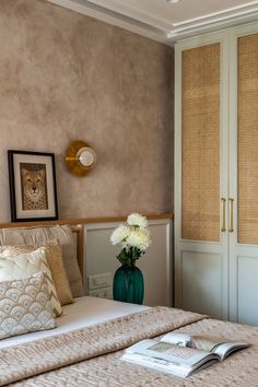 a bedroom with beige walls and white bedding has a green vase with flowers in it