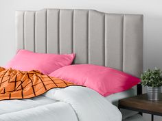 a bed with pink and orange pillows on it next to a wooden table in front of a white wall