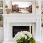 a living room with white furniture and a painting on the fireplace mantel above it