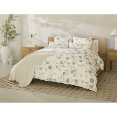 a bed with white and blue flowers on it in a room next to two nightstands