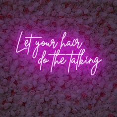 a pink neon sign that says let your hair do the talking in front of flowers