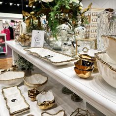 gold and white dishes are on display in a store, with other items behind them