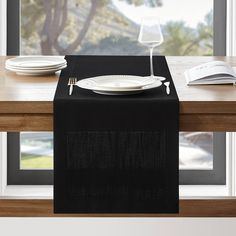 a black table runner with white plates and silverware on it in front of a window