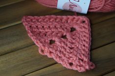 a pink crocheted triangle sits on a wooden surface