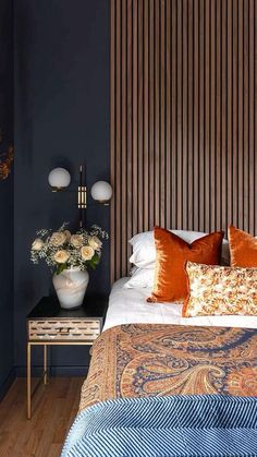 a bed with orange and blue pillows on top of it next to a night stand