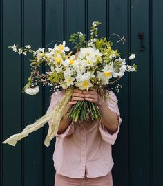 a woman holding a bouquet of white and yellow flowers in front of her face while standing next to a green door