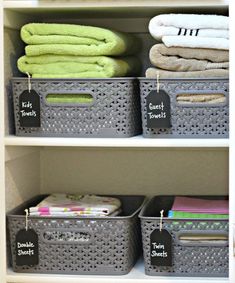 the shelves have baskets with labels on them and some folded towels in bins next to each other