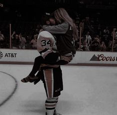 two people are hugging on the ice during a hockey game in front of an audience