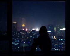 a person sitting on a window sill looking out at the city lights in the distance