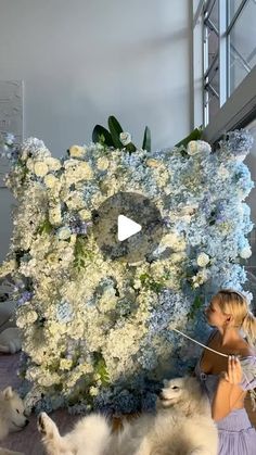 a woman standing next to two dogs in front of a large bouquet of white and blue flowers