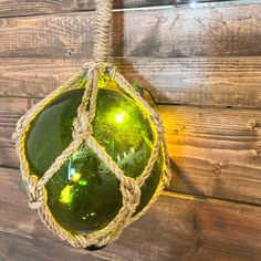 a green glass ornament hanging from a rope on a wooden wall with wood planks