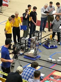 a group of men standing around each other in front of a camera set up on a basketball court