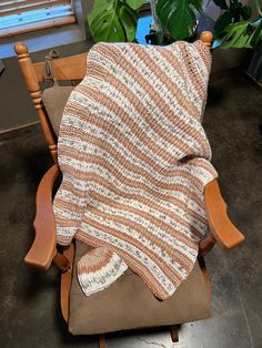 a chair with a blanket on it in front of a potted plant and window