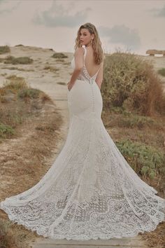 a woman in a white wedding dress standing on a dirt path near the ocean with her back to the camera