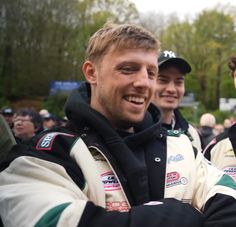 two men standing next to each other with their arms crossed and one man in the background smiling