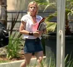 a woman is walking down the street while holding a book in her hand and looking at the camera