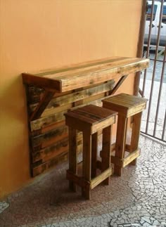 a wooden bench sitting next to a wall with two stools on top of it