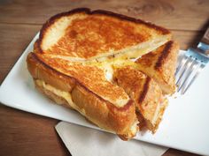 a grilled cheese sandwich on a white plate with a fork and knife next to it