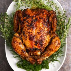 a roasted chicken on a white plate with fresh herbs