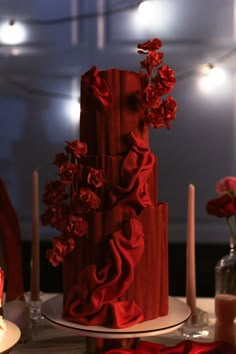 a three tiered red cake with flowers on top and candles in the back ground