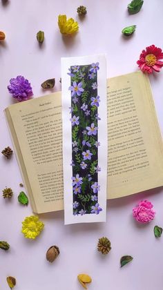 an open book laying on top of a table covered in flowers and leaves next to a paper strip