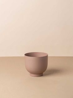 a pink bowl sitting on top of a table next to a white wall and floor