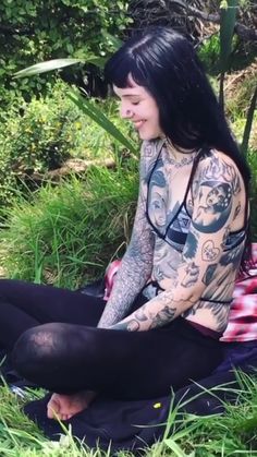 a woman with tattoos sitting in the grass