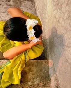 a woman in a yellow dress is sitting on some steps with flowers in her hair