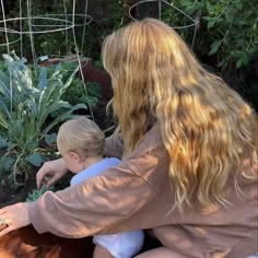 a woman kneeling down next to a little boy in front of a garden filled with plants