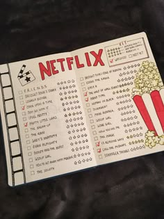 an open book with a movie list on it and a cup of popcorn next to it