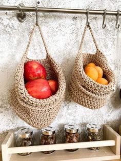 two baskets filled with apples hanging from hooks next to spice jars on a shelf in front of a wall