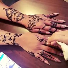 two hands with henna tattoos on them sitting next to each other and a cell phone