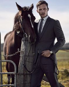 a man in a suit and tie standing next to a horse near a wooden post