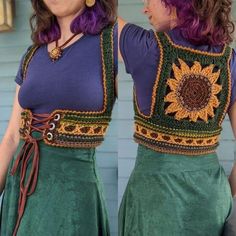 a woman with purple hair wearing a green skirt and sunflower top in front of a blue house